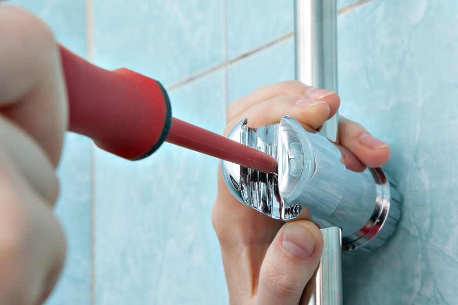 Residential plumbing repair close-up of hands handyman with red phillips screwdriver install adjustable shower slide rail bar bracket.